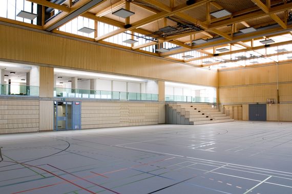 Die grosse Sporthalle mit dem grauen Turnboden und einer ausgezogener Tribüne im Hintergrund.