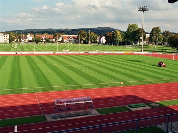 Der Platz Nr. 1 mit der roten Tartarbahn und der Leichtathletikanlage. Auf der Wiese fährt der Rasenmäher und zieht die Bahnen.