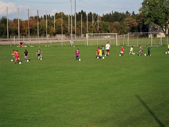 Auf dem Fussballplatz sind kleinere Kinder im Fussballtraining und versuchen mit dem Ball zu spielen.