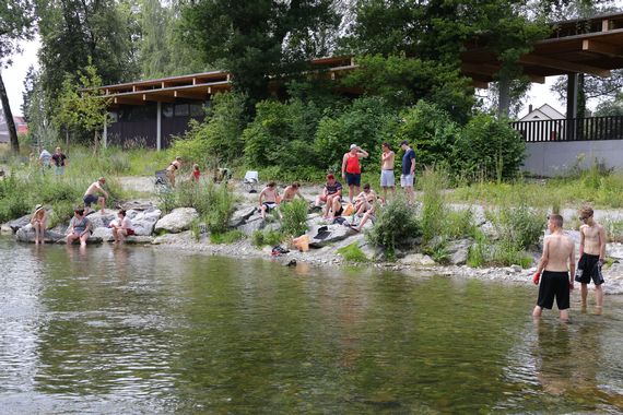 Viele Personen welche bei sommerlichen Temperaturen an der Murg sitzen. Einige Personen kühlen sich auch im Wasser ab.