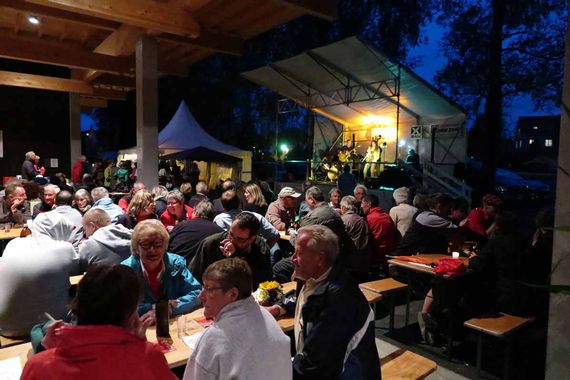Ein Anlass beim Unerstand des Pavillons, als es schon dunkel war. Der Unterstand ist hell erleuchtet und im Hintergrund ist eine kleine Bühne zu sehen.