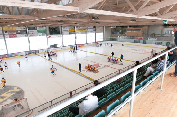 Ein Blick in die Eishalle von der Tribüne. Auf dem Eis sind Personen zu sehen, die das Eis am richten sind für ein Training.