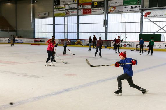 Das Halleneis während des öffentlichen Eislaufes mit Personen, welche Eishockeystöcke in der Hand haben.