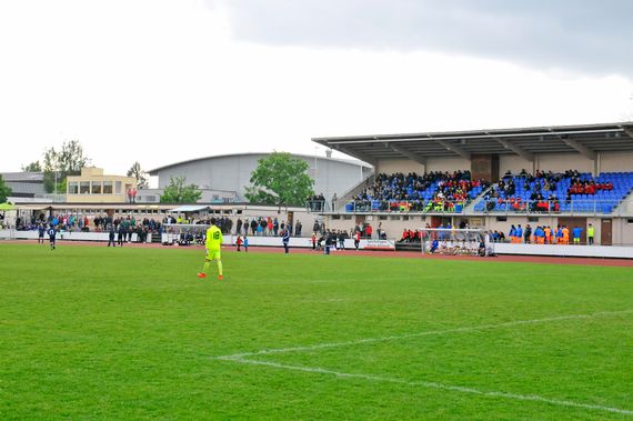 Der Fussballclub an einem Match mit gefüllter Tribüne und Personen, welche an den Banden stehen.