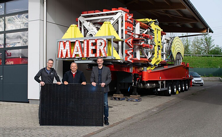 Hans Peter Maier, Peter Wieland und Fabrizio Hugentobler stehen vor einer Fahrgeschäft. Sie halten ein Teil dre PV-Anlage in den Händen.